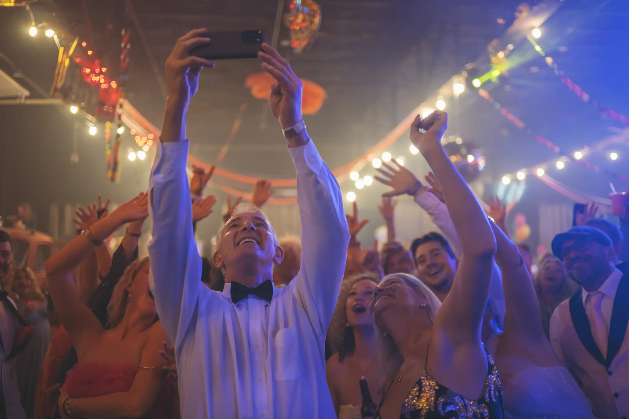 Guests smiling and raising their hands beneath string lights at White Squirrel's prom