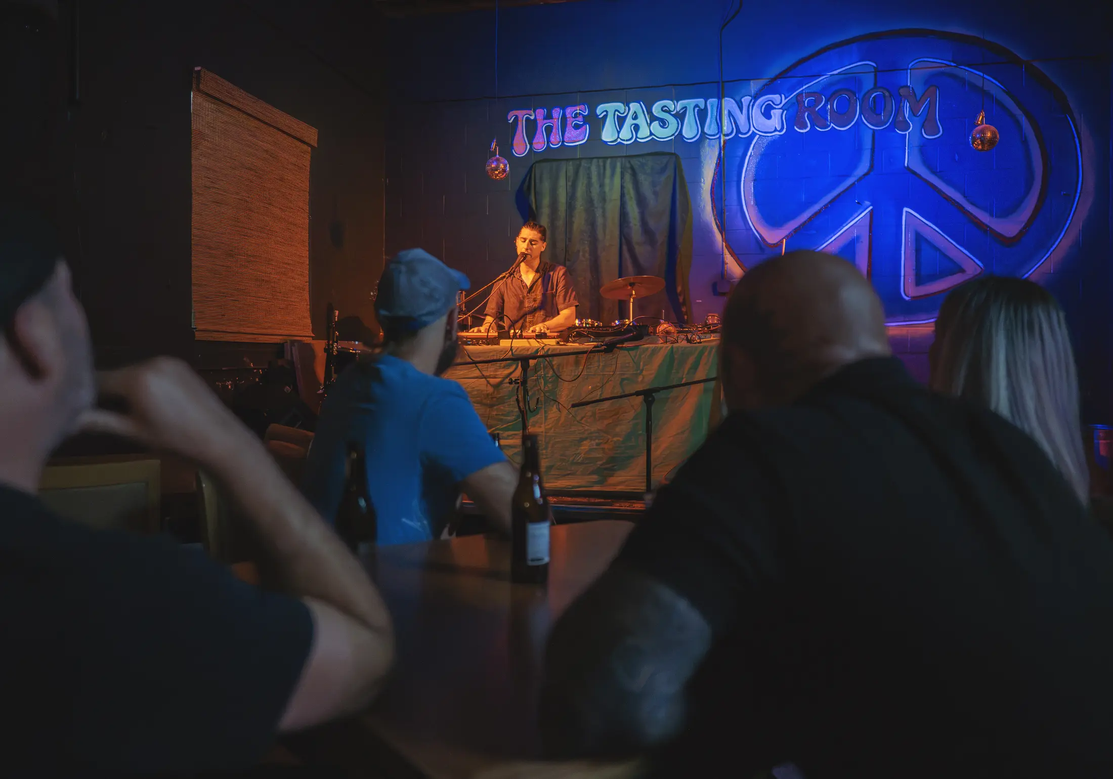 An audience listening to a performer under The Tasting Room sign